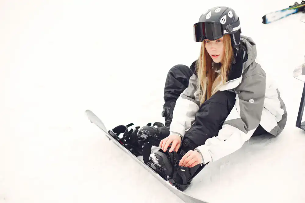 Snowboarder strapping into bindings on a snowy peak